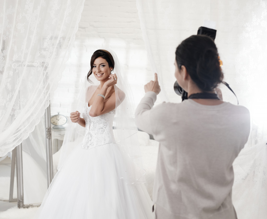 Female photographer photographing beautiful happy bride indoors.