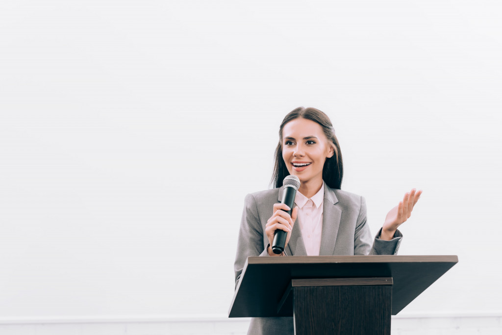 A confident businesswoman using a microphone on a podium to present a talk