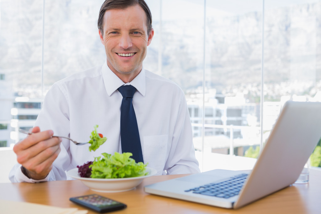 An employee is eating a salad while in front of his laptop