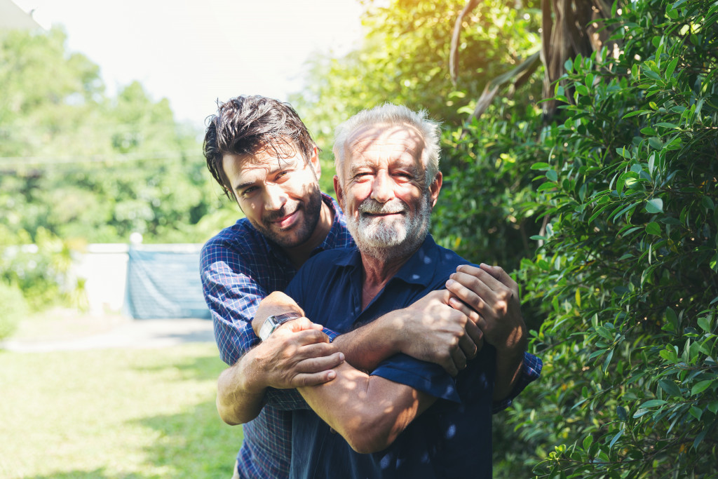 An adult man hugs his elderly father while they are out in their yard