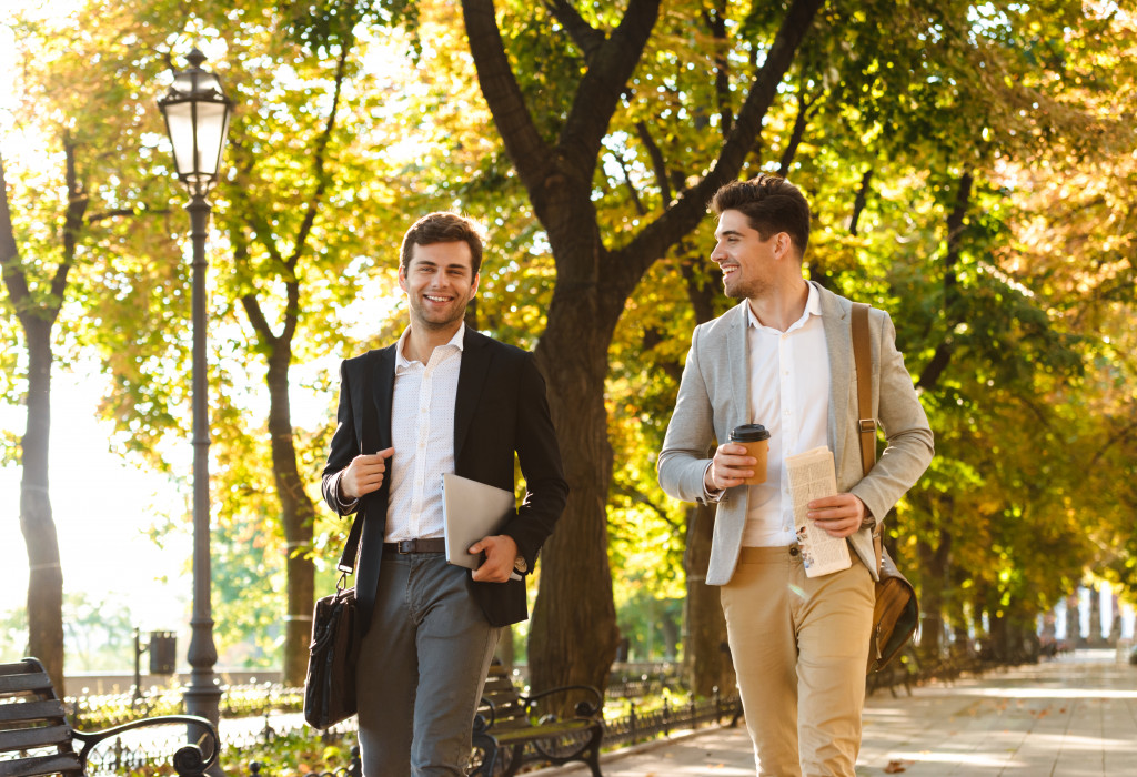 Two handsome businessmen walking with coffee in a sunny park