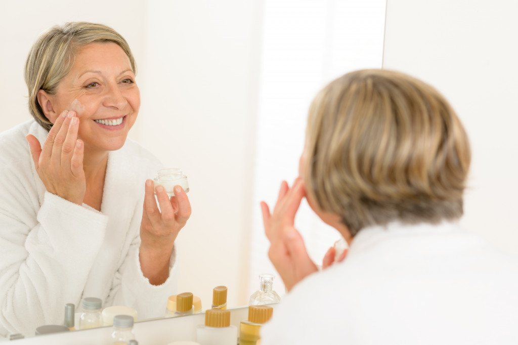a woman looking in the mirror and applying skincare product on her face